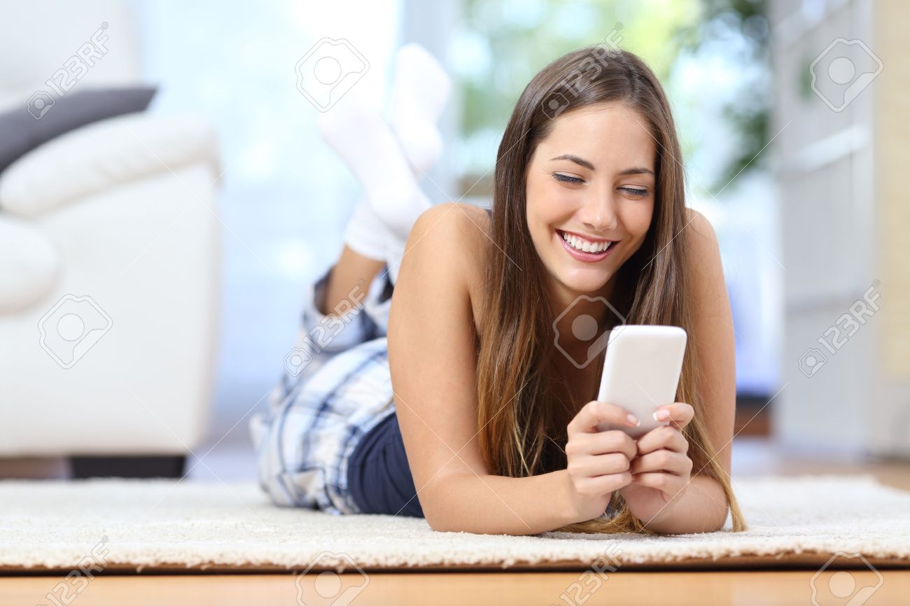 Happy tiener sms op de mobiele telefoon liggend op een tapijt in ... Tapijt voor de woonkamer grijze