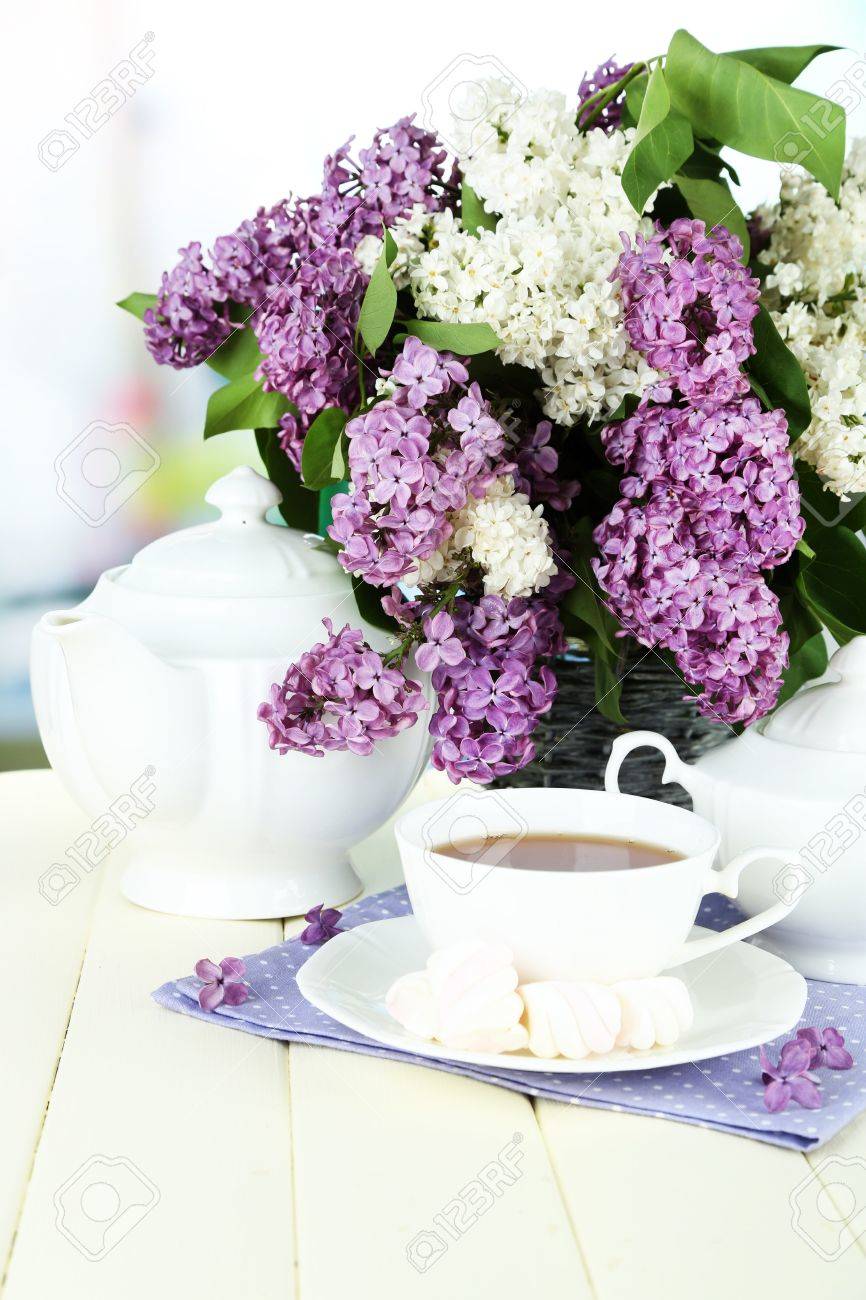 Foto de archivo , Composición con hermosas flores de color lila, servicio de té en la mesa de madera sobre fondo brillante