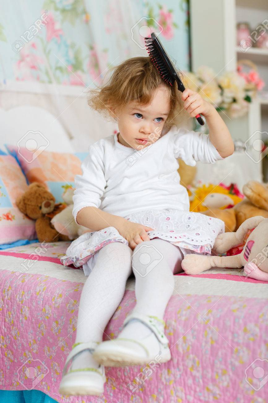 Kleines mädchen, das kämmen der haare sitzt auf dem bett im ... Kleines kinderzimmer für 2