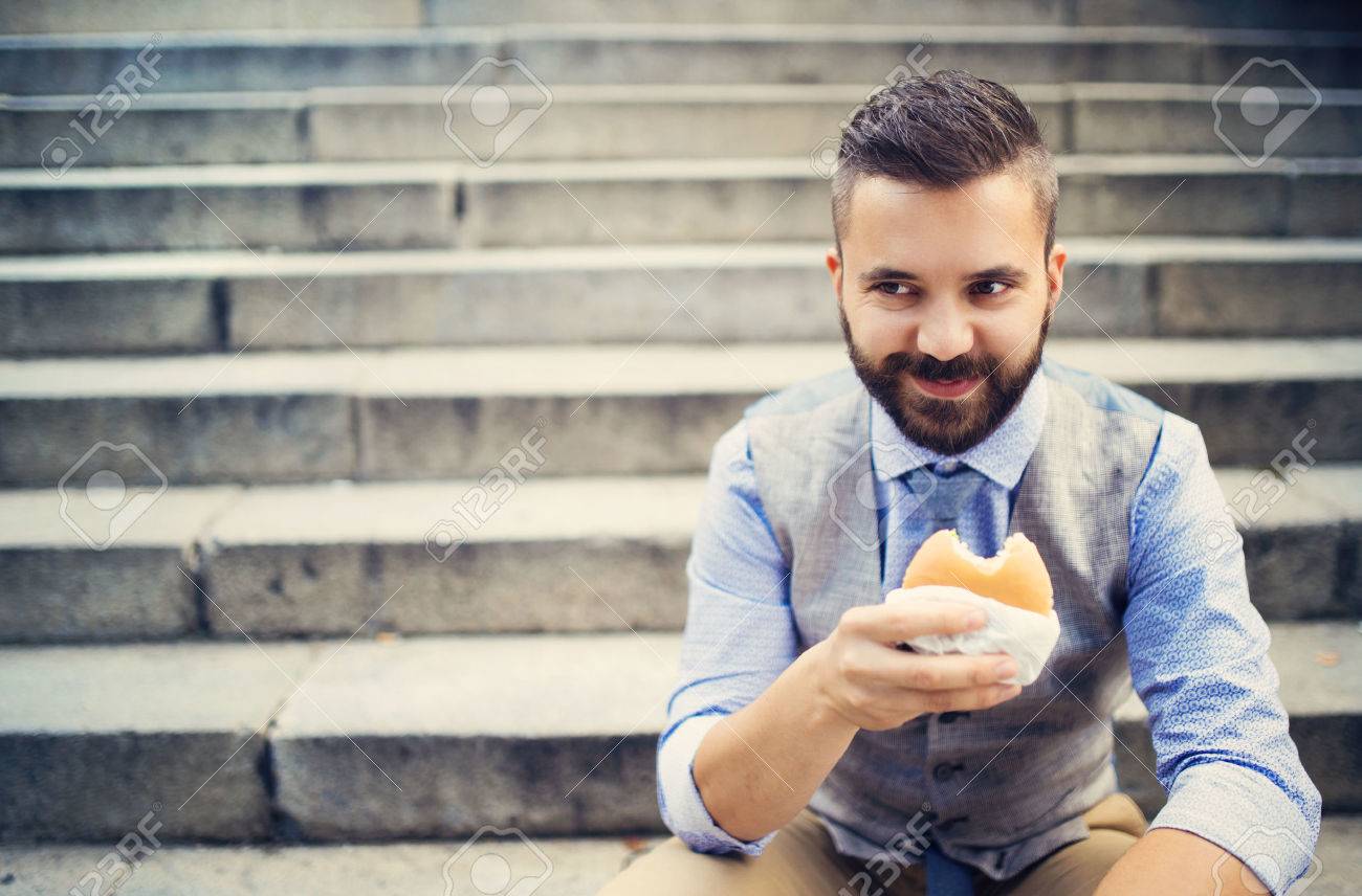 31963317-Modern-hipster-businessman-having-lunch-break-sitting-on-stairs-in-town-center-and-eating-burger-Stock-Photo.jpg