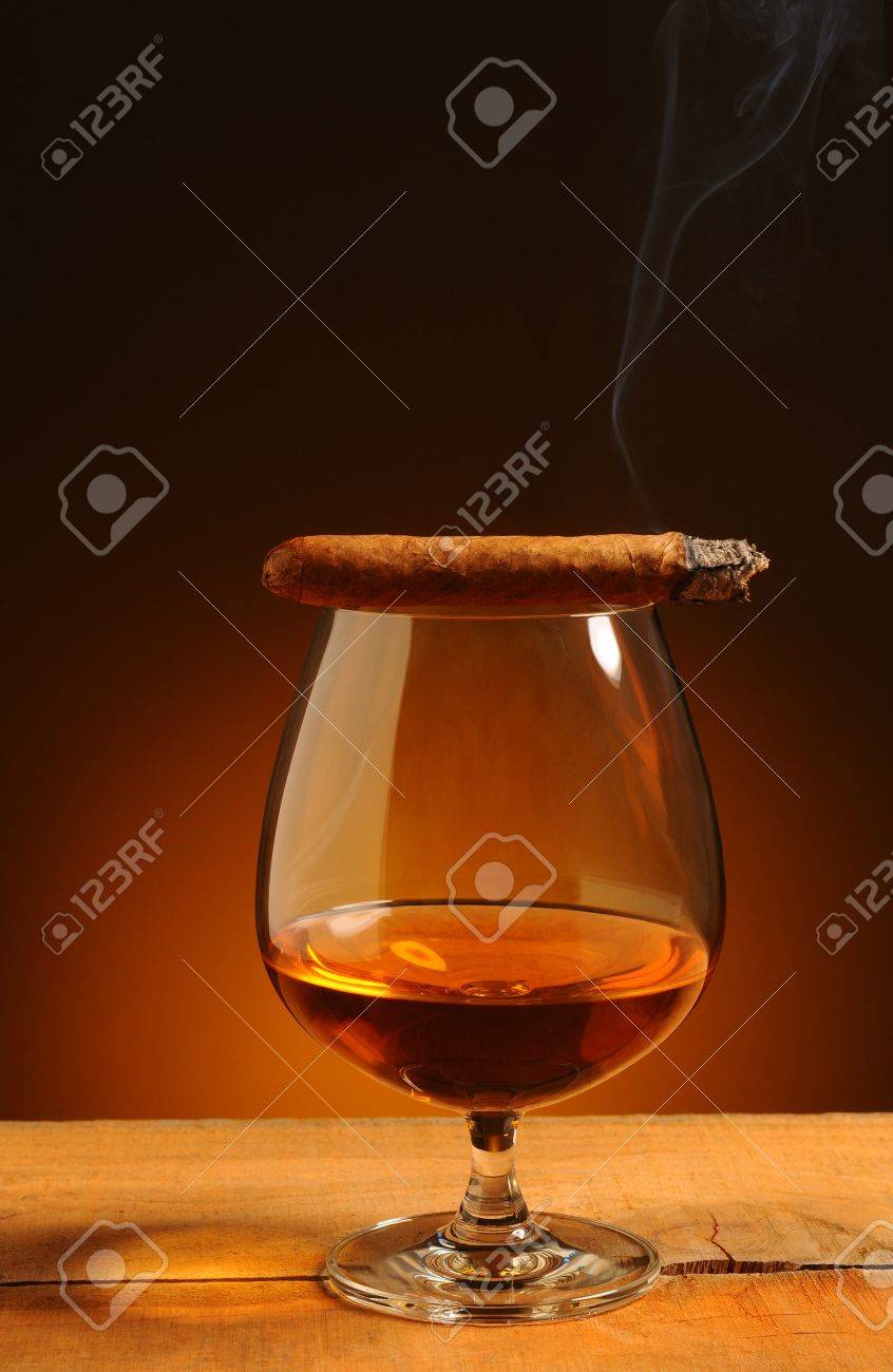 Vetro brandy con un sigaro acceso sul suo bordo su un fondo caldo ...