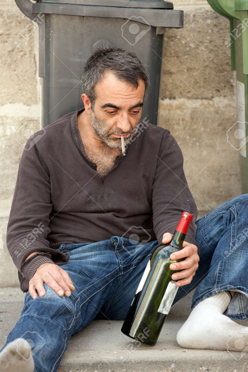 7617185-drunk-man-siitng-on-sidewalk-near-trashcan-in-city-street-Stock-Photo.jpg