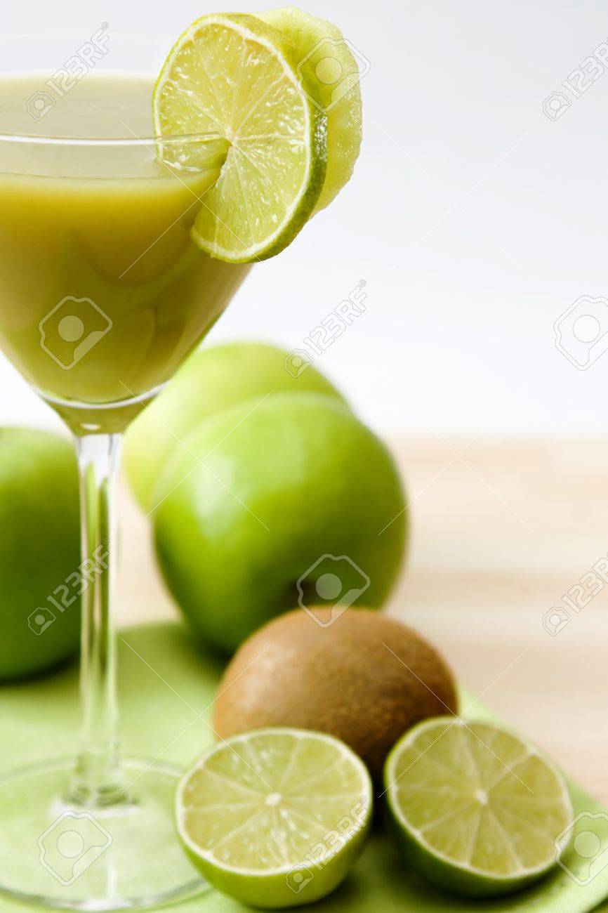 Close,up image of a glass with a green fruit juice and lime and kiwi