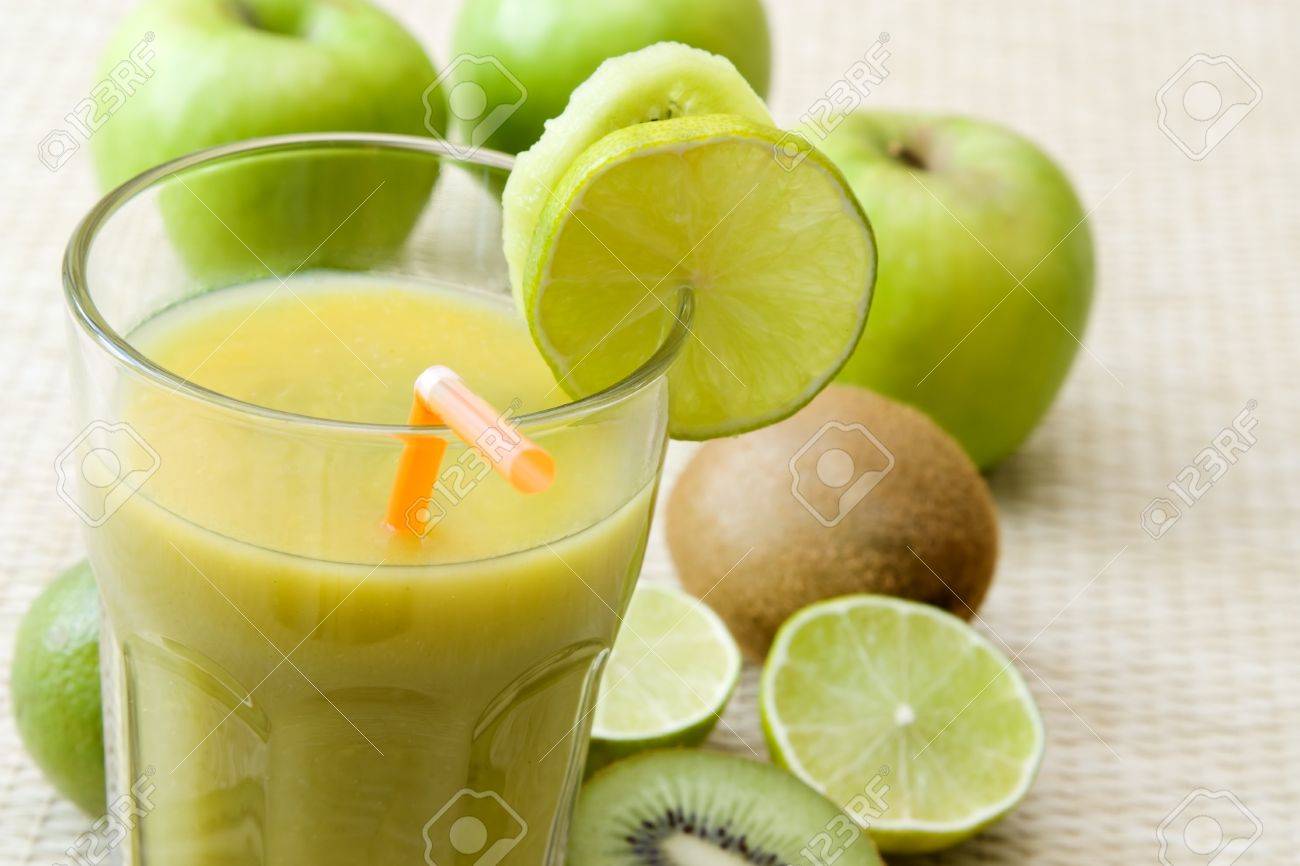 Close,up image of a glass with a green fruit juice and lime and kiwi