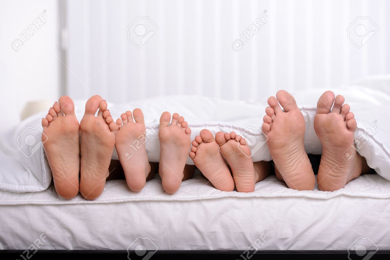 Moeder, vader en twee kinderen liggen op bed met witte lakens ...