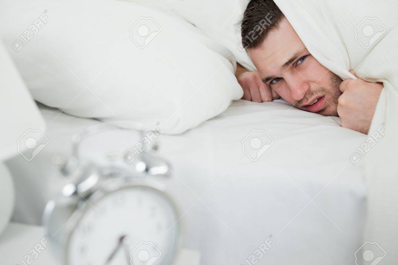 Verärgert mann hält sich die ohren, während sein wecker klingelt ... Schlafzimmer mann