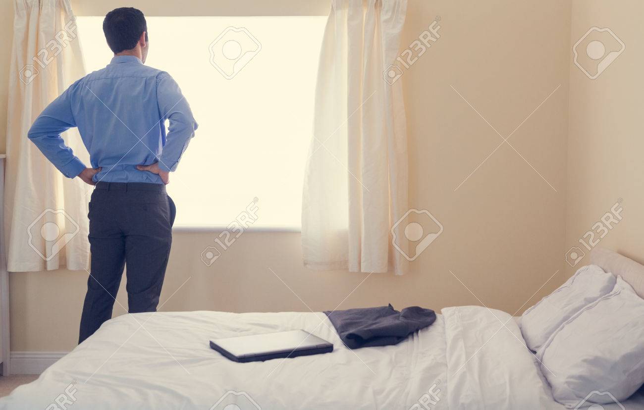 Vista posteriore di un uomo in piedi davanti a una finestra e ... Camera letto uomo