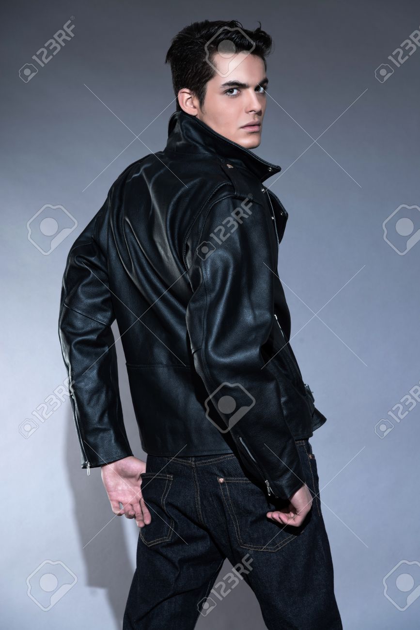 Retro rock and roll 50s fashion man with dark grease hair. Wearing black leather jacket and jeans. Studio shot against grey