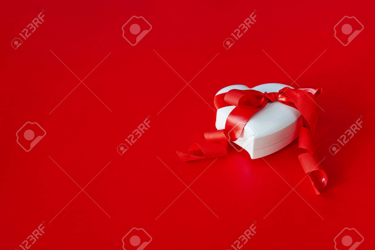 バレンタインの日のための豪華な贈り物 ハートの形をした白い箱は 赤い背景に赤いリボンと結ばれます の写真素材 画像素材 Image