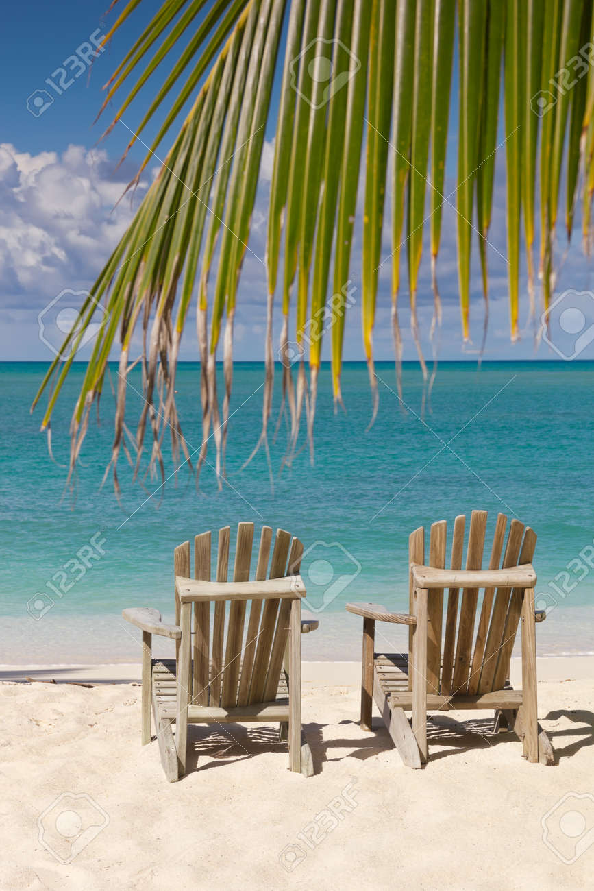 Beach chairs on white sand beach with cloudy blue sky and sun