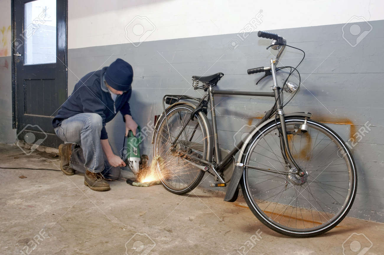 Bicycle thief busy breaking the lock with a portable grinding machine - 6552729 Bicycle thief busy breaking the lock with a portable grinding machine - 6552729