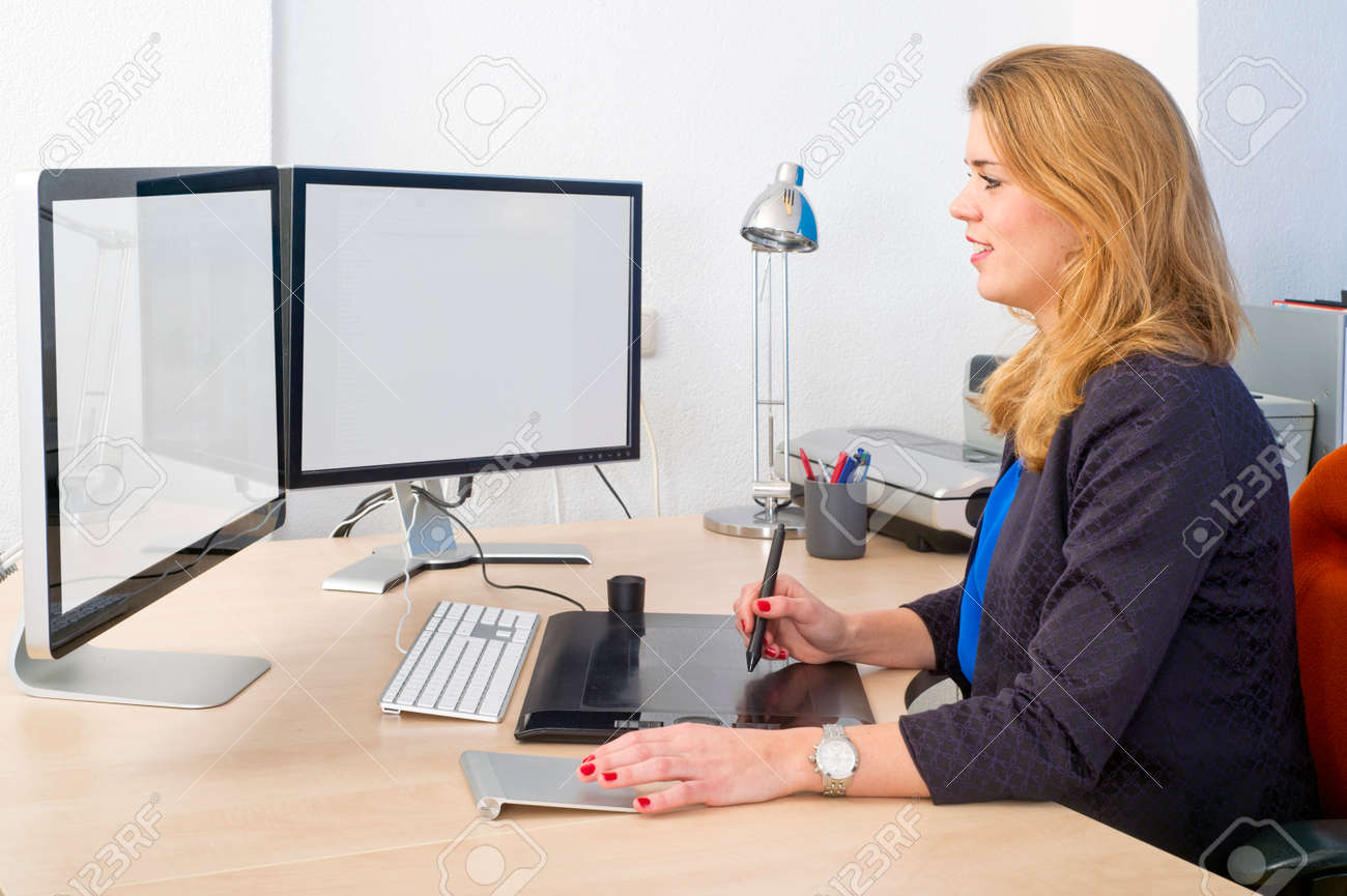 young woman sitting behind a large desk and a dual screen computer