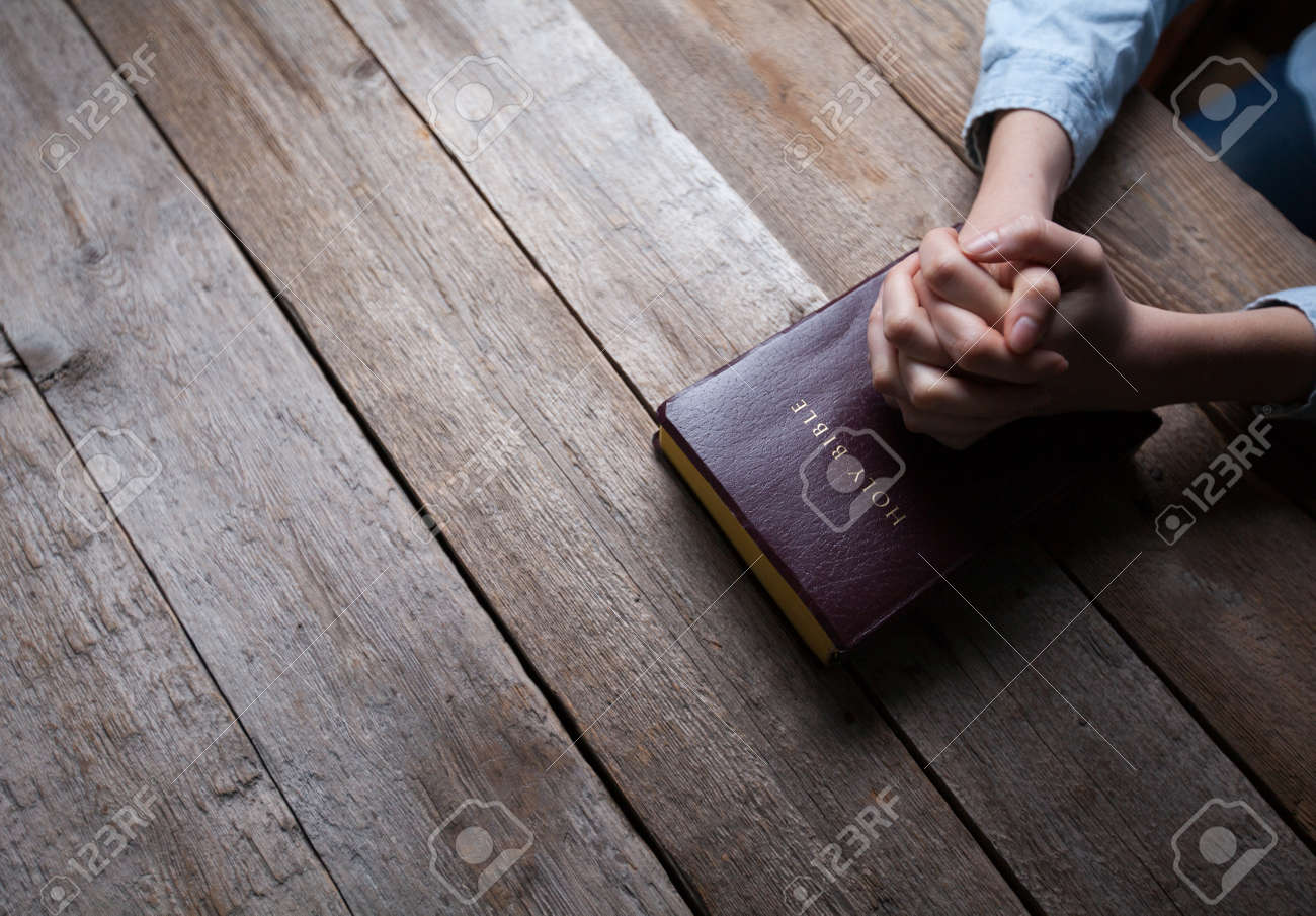 hands praying with a bible in a dark over wooden table - 54964153 hands praying with a bible in a dark over wooden table - 54964153