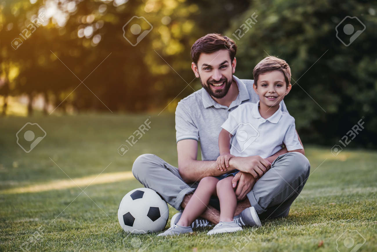 緑の草が茂った芝生でサッカーをプレイしている彼の小さなかわいい太陽とハンサムなお父さん の写真素材 画像素材 Image