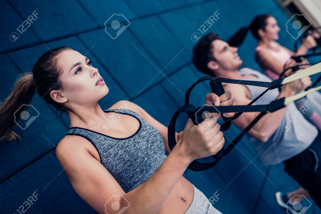 스포츠 사람들의 그룹은 TRX와 함께 야외 훈련을하고 있습니다. 몸 전체 저항 운동. 두 매력적인 젊은 여성과 잘 생긴 남자는  체육관에서 운동하고 있습니다. 로열티 무료 사진, 그림, 이미지 그리고 스톡포토그래피. Image 90078221