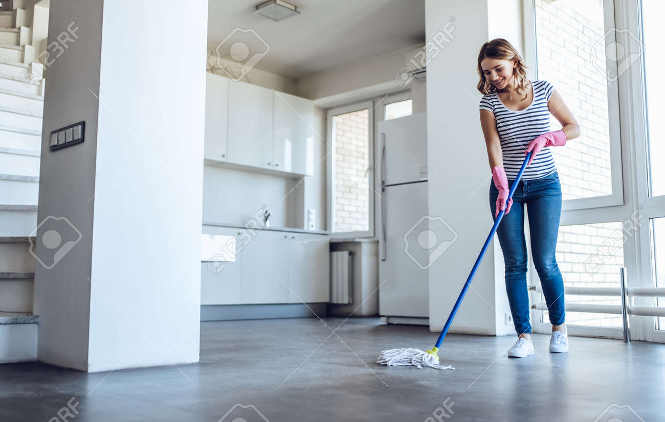 Belle jeune femme lave le sol tout en faisant le ménage à la maison Belle jeune femme lave le sol tout en faisant le ménage à la maison