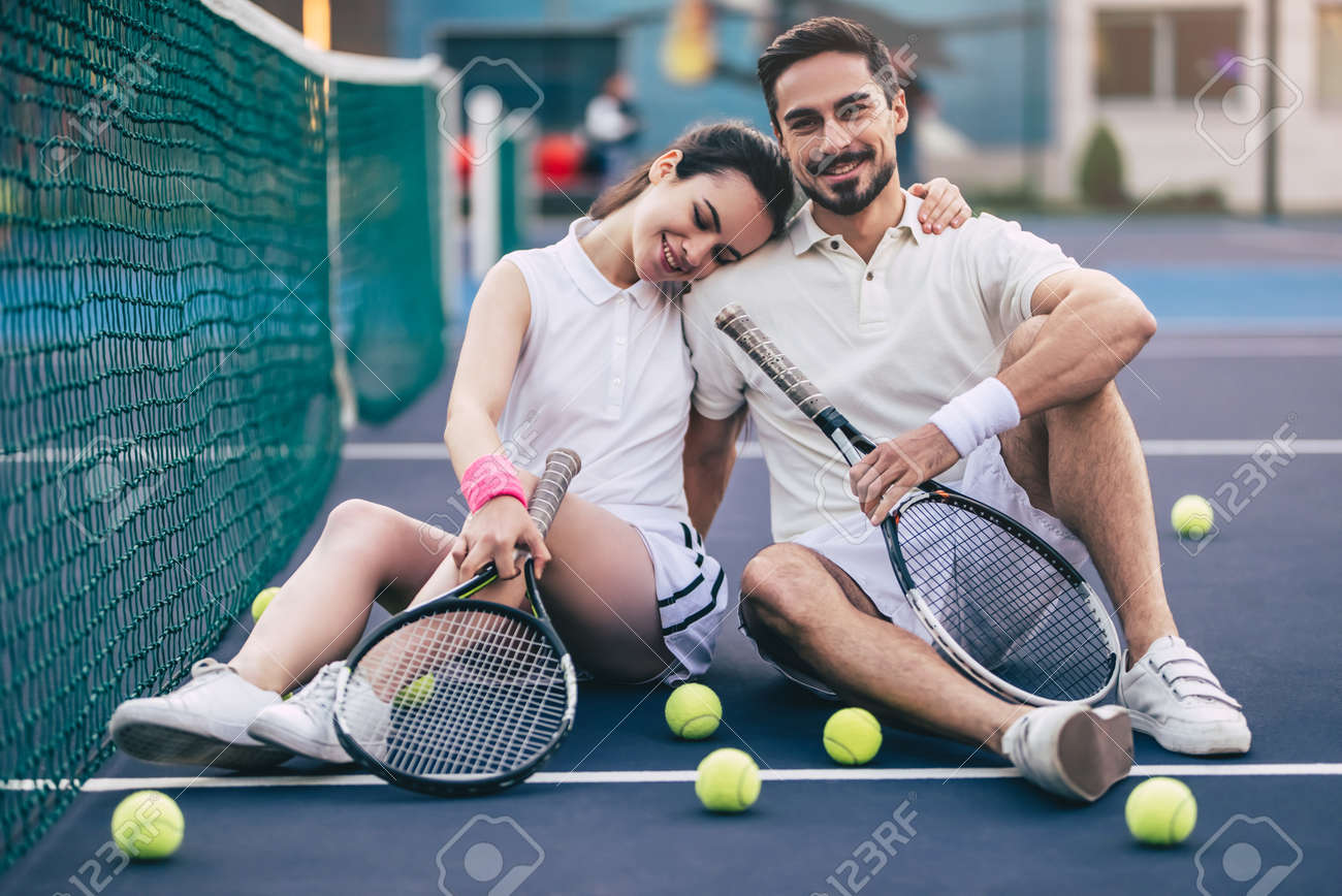 Young couple is sitting on tennis court. Handsome man and attractive woman are playing tennis. - 91996713 Young couple is sitting on tennis court. Handsome man and attractive woman are playing tennis. - 91996713