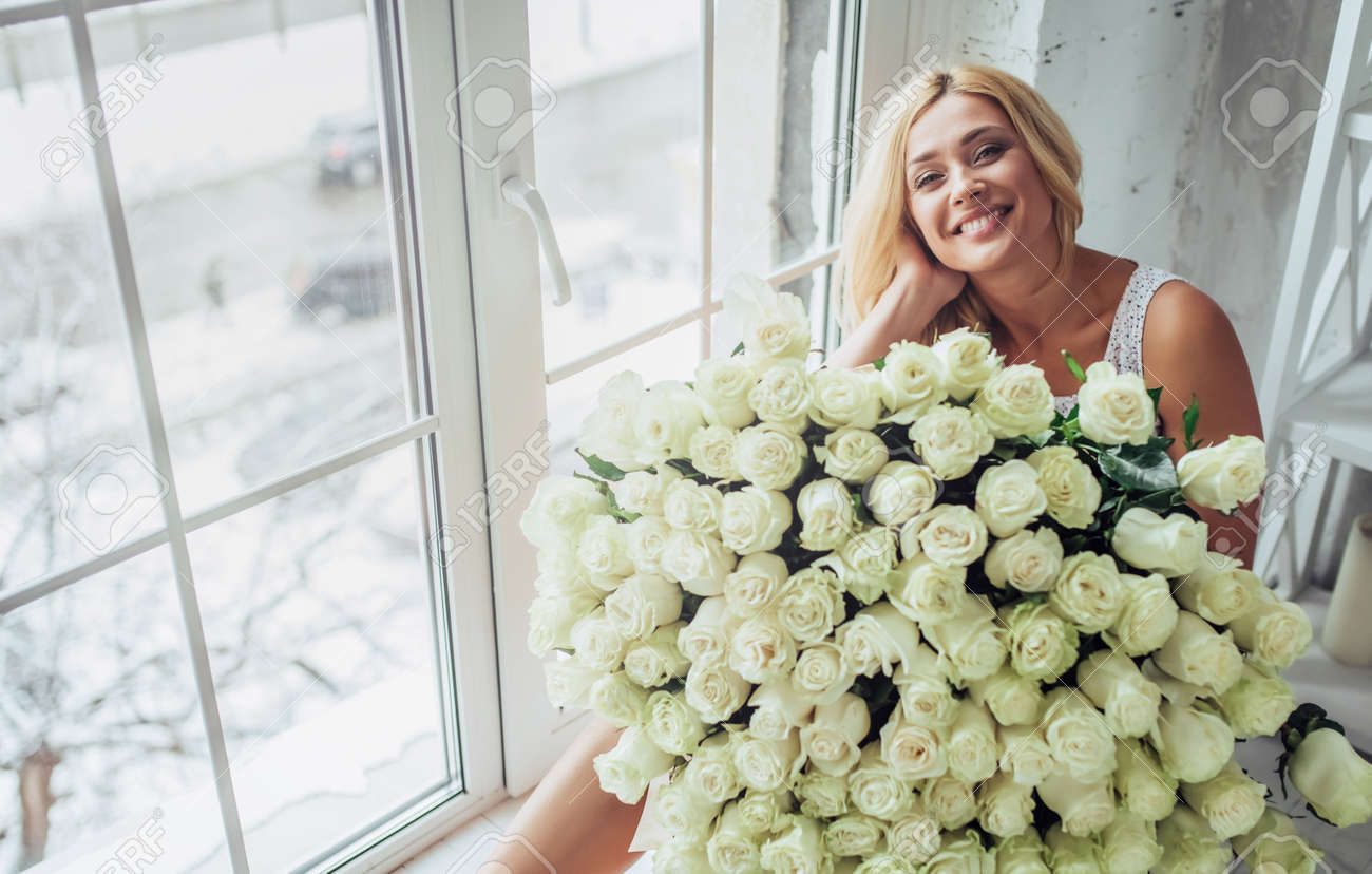 何百もの白いバラの花束を持つ魅力的な若い女性は 自宅で時間を過ごしています の写真素材 画像素材 Image