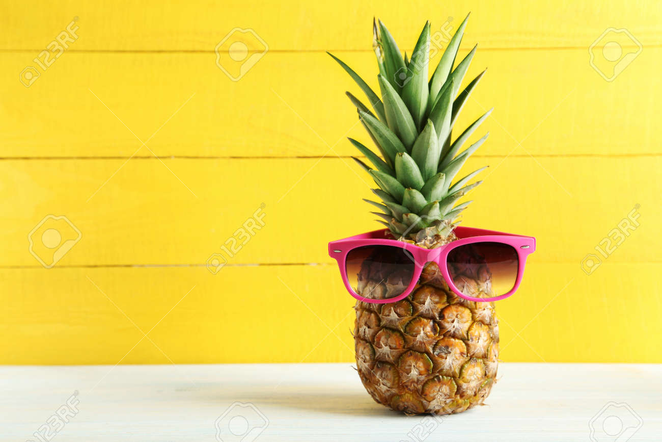Ripe pineapple with sunglasses on a white wooden table - 51480514 Ripe pineapple with sunglasses on a white wooden table - 51480514
