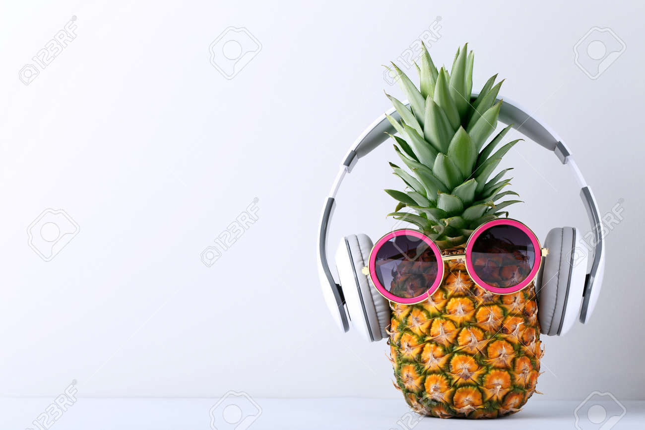 Ripe pineapple with headphones on grey background - 80205577 Ripe pineapple with headphones on grey background - 80205577