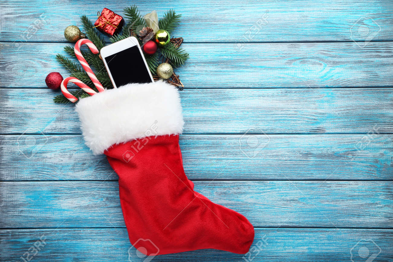 Red stocking with fir-tree branches and smartphone on wooden table - 90614371 Red stocking with fir-tree branches and smartphone on wooden table - 90614371