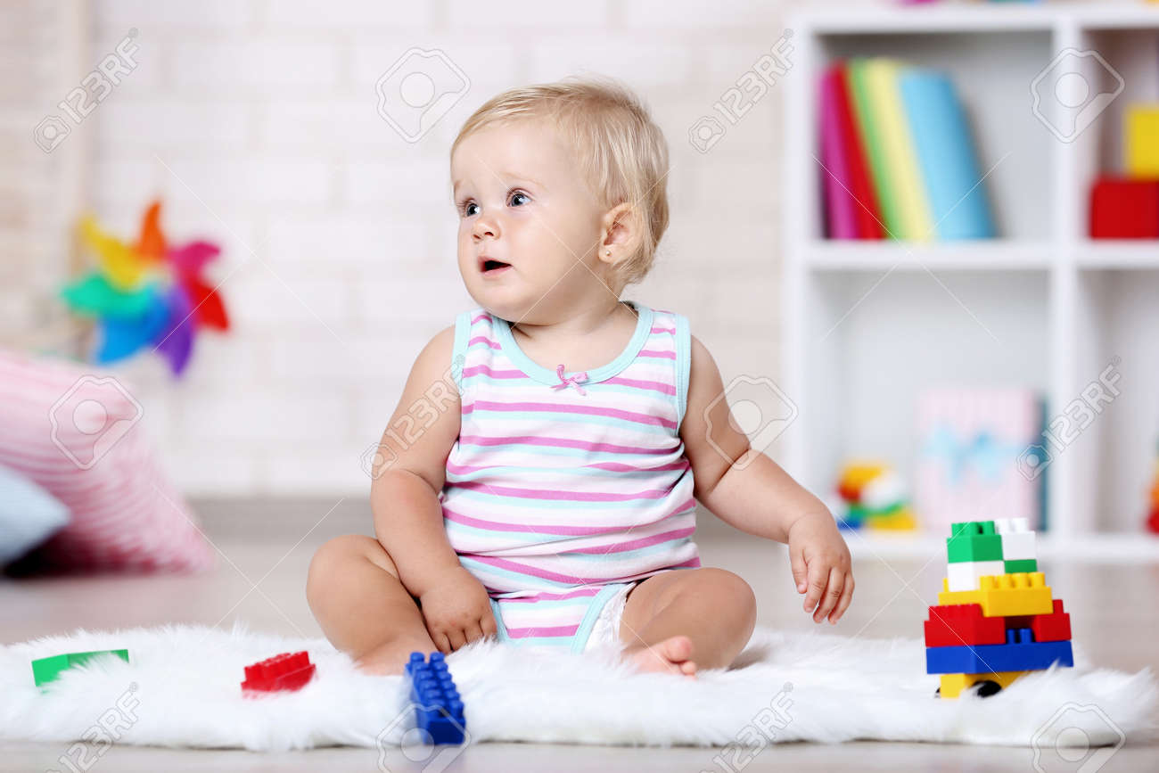 Baby girl sitting on white carpet with toys - 120768145 Baby girl sitting on white carpet with toys - 120768145