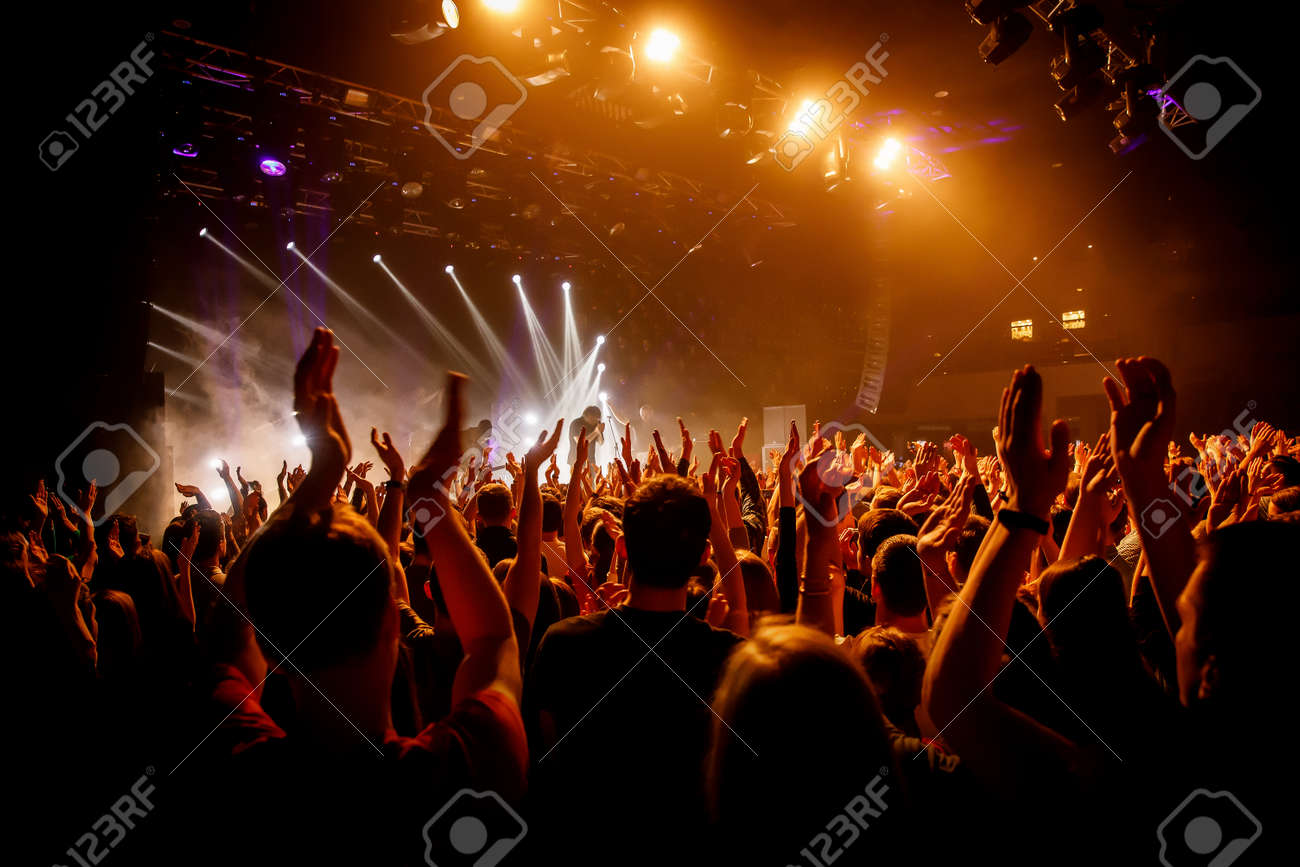Crowd on music show, happy people with raised hands. Orange stage light - 120665550 Crowd on music show, happy people with raised hands. Orange stage light - 120665550