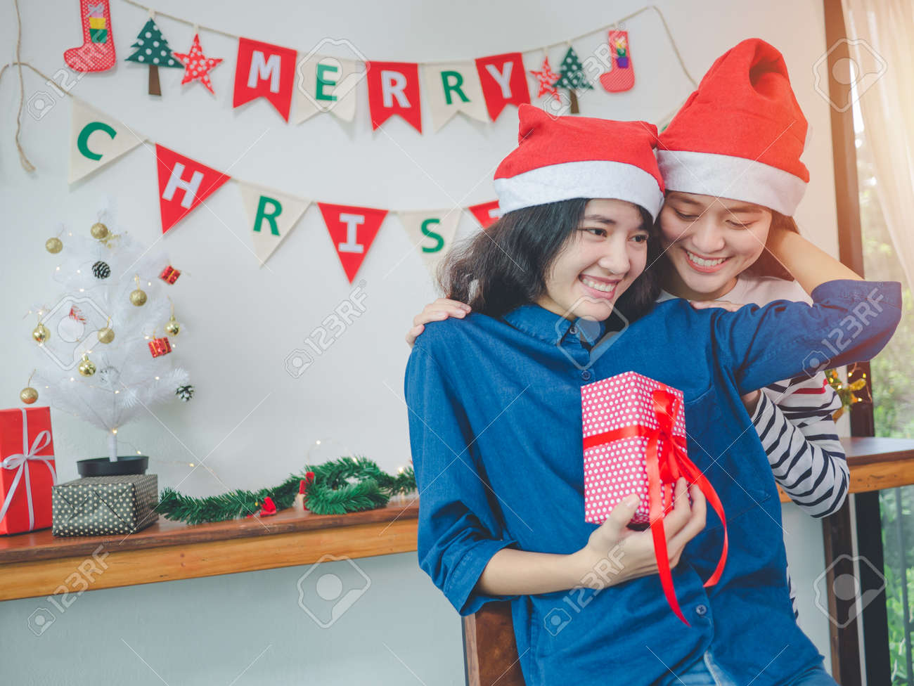 クリスマスパーティーでギフトボックスを保持している2人のアジアの女性レズビアンカップルは クリスマスツリーの装飾品を持っています の写真素材 画像素材 Image