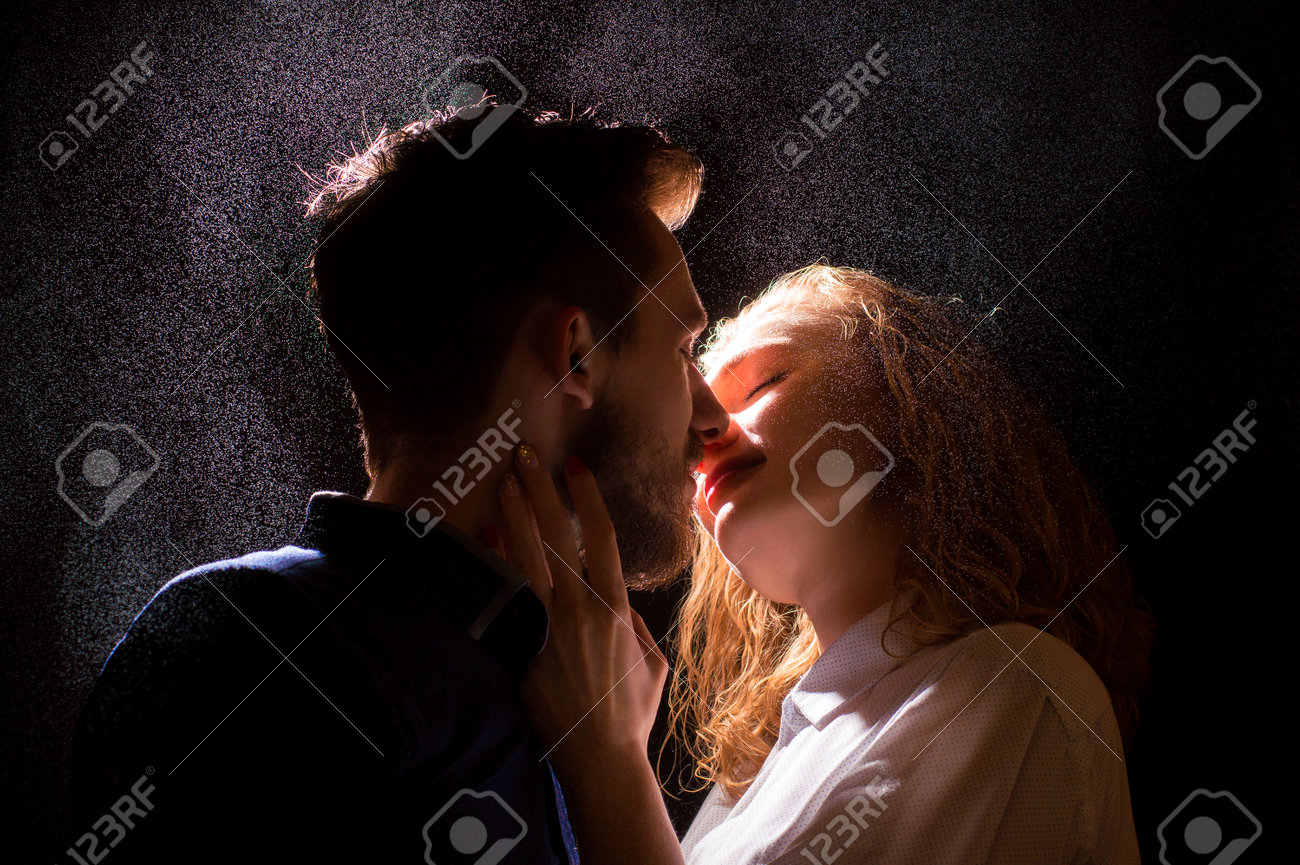 Close sensual pre-kiss moment with rain-like droplets, intense eye-closed surrender and desire in dramatic light