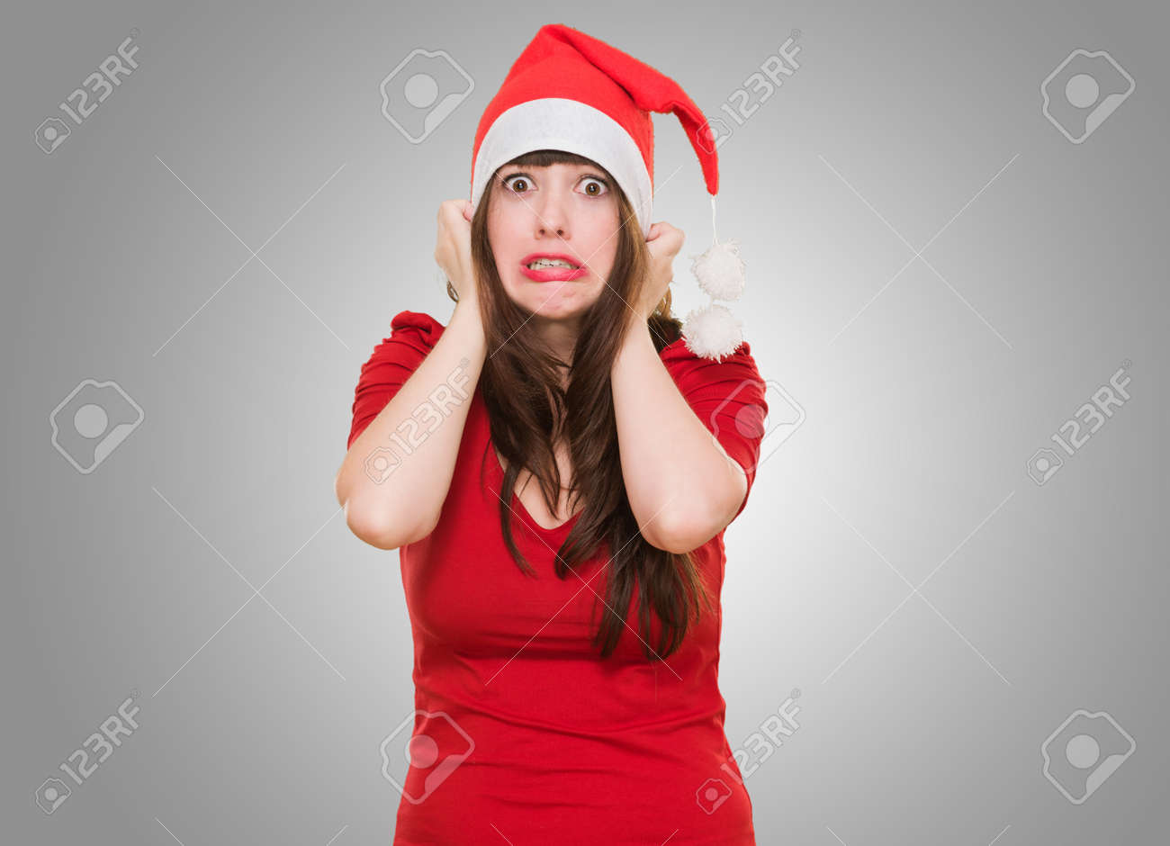 scared woman wearing a christmas hat against a grey background - 16290879 scared woman wearing a christmas hat against a grey background - 16290879