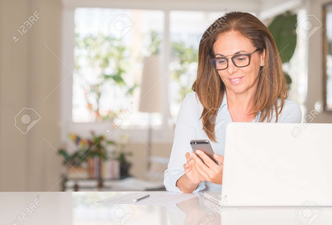Middle age woman using smartphone and laptop, indoor - 104066520 Middle age woman using smartphone and laptop, indoor - 104066520