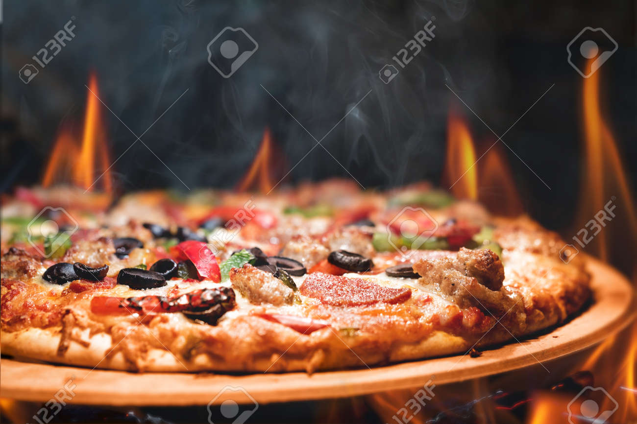 Supreme meat and vegetable pizza on stone in wood-fired oven with open flames - 62686386 Supreme meat and vegetable pizza on stone in wood-fired oven with open flames - 62686386