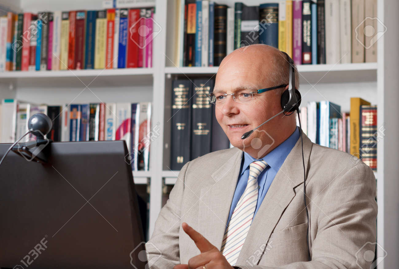 Friendly businessman with headphones in front of a computer with camera - 25745228 Friendly businessman with headphones in front of a computer with camera - 25745228