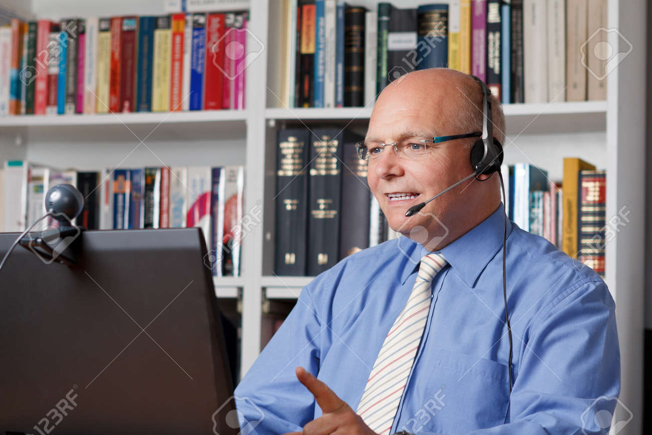 Friendly smiling man with headphones, notebook and webcam telephoning - 25746398 Friendly smiling man with headphones, notebook and webcam telephoning - 25746398