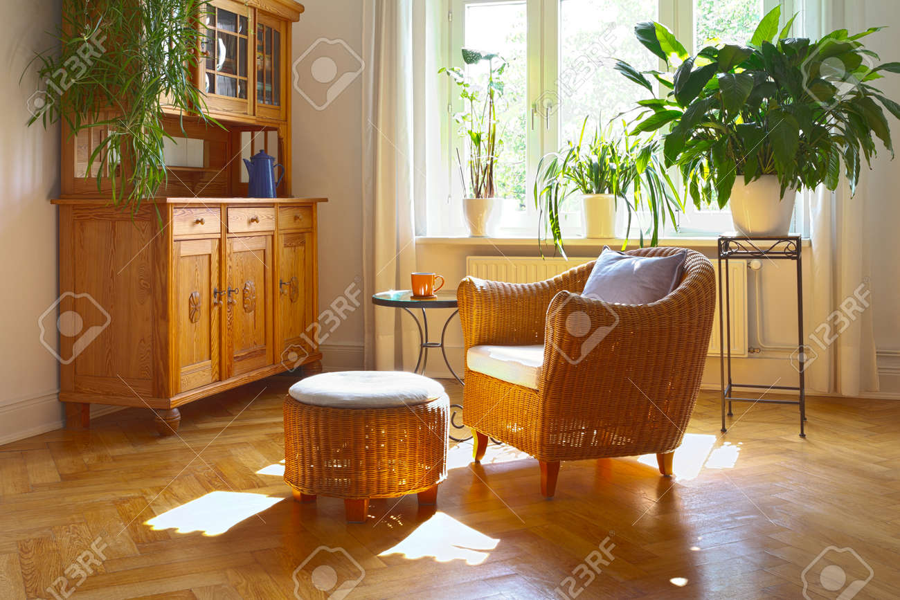 Sunny living room in warm colors with wicker armchair and stool, antique cupboard and plants - 42781803 Sunny living room in warm colors with wicker armchair and stool, antique cupboard and plants - 42781803