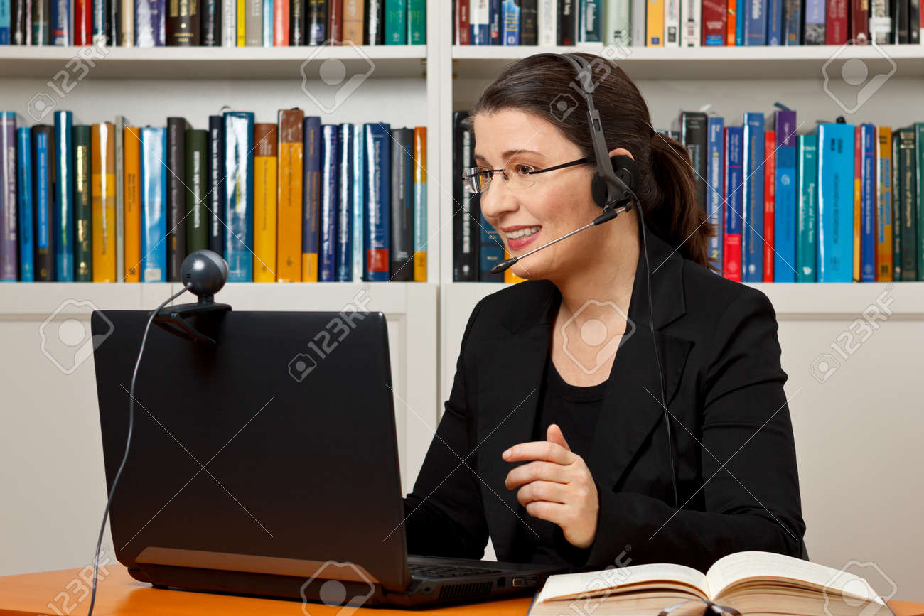 Mature woman with headset, laptop and webcam in front of a lot of books, giving online legal advice via a video call - 50496511 Mature woman with headset, laptop and webcam in front of a lot of books, giving online legal advice via a video call - 50496511