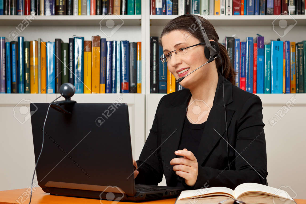 Female tutor or teacher with headset, computer and camera in her office talking with a student via video telephony, skype - 50497032 Female tutor or teacher with headset, computer and camera in her office talking with a student via video telephony, skype - 50497032