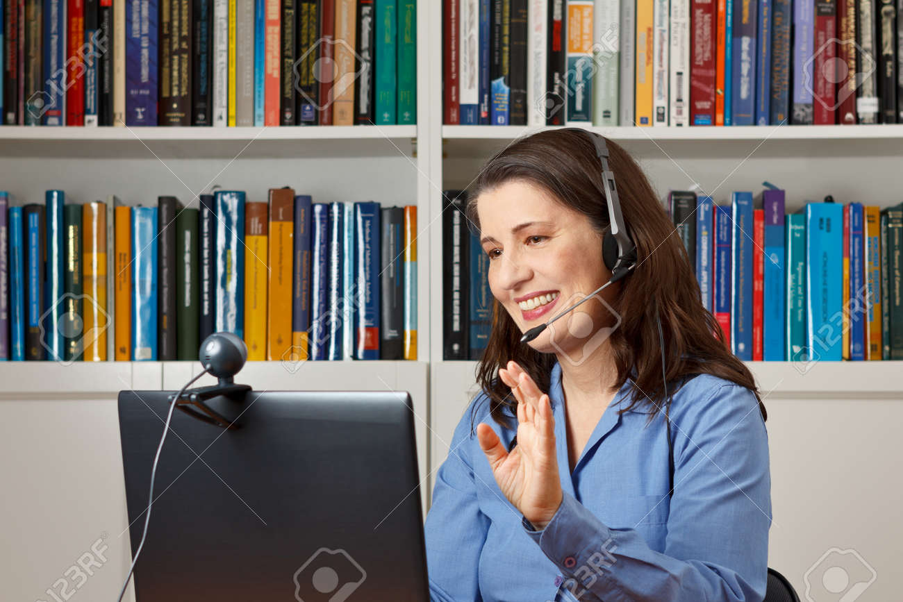 Smiling woman in her office with laptop, camera and headset telephoning with her children via the internet - 50497036 Smiling woman in her office with laptop, camera and headset telephoning with her children via the internet - 50497036