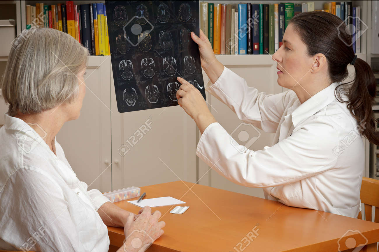 2 women in a surgery: middle aged doctor in lab coat showing her senior patient magnetic resonance images of her head - 65805360 2 women in a surgery: middle aged doctor in lab coat showing her senior patient magnetic resonance images of her head - 65805360