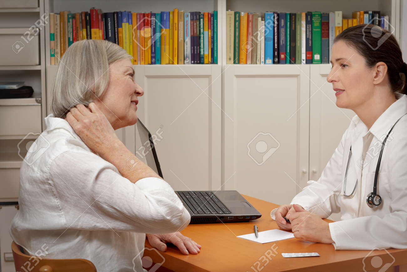 Senior female patient consulting middle aged doctor because of strong neck pain caused by muscular tension - 65805385 Senior female patient consulting middle aged doctor because of strong neck pain caused by muscular tension - 65805385