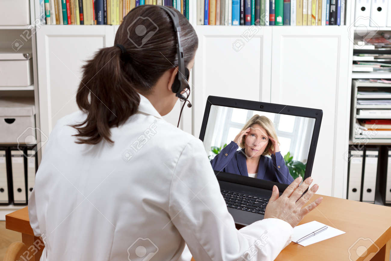Female doctor or pharmacist in her surgery office with headset in front of her computer talking via video chat with a patient, telling her to take things easy - 72652961 Female doctor or pharmacist in her surgery office with headset in front of her computer talking via video chat with a patient, telling her to take things easy - 72652961
