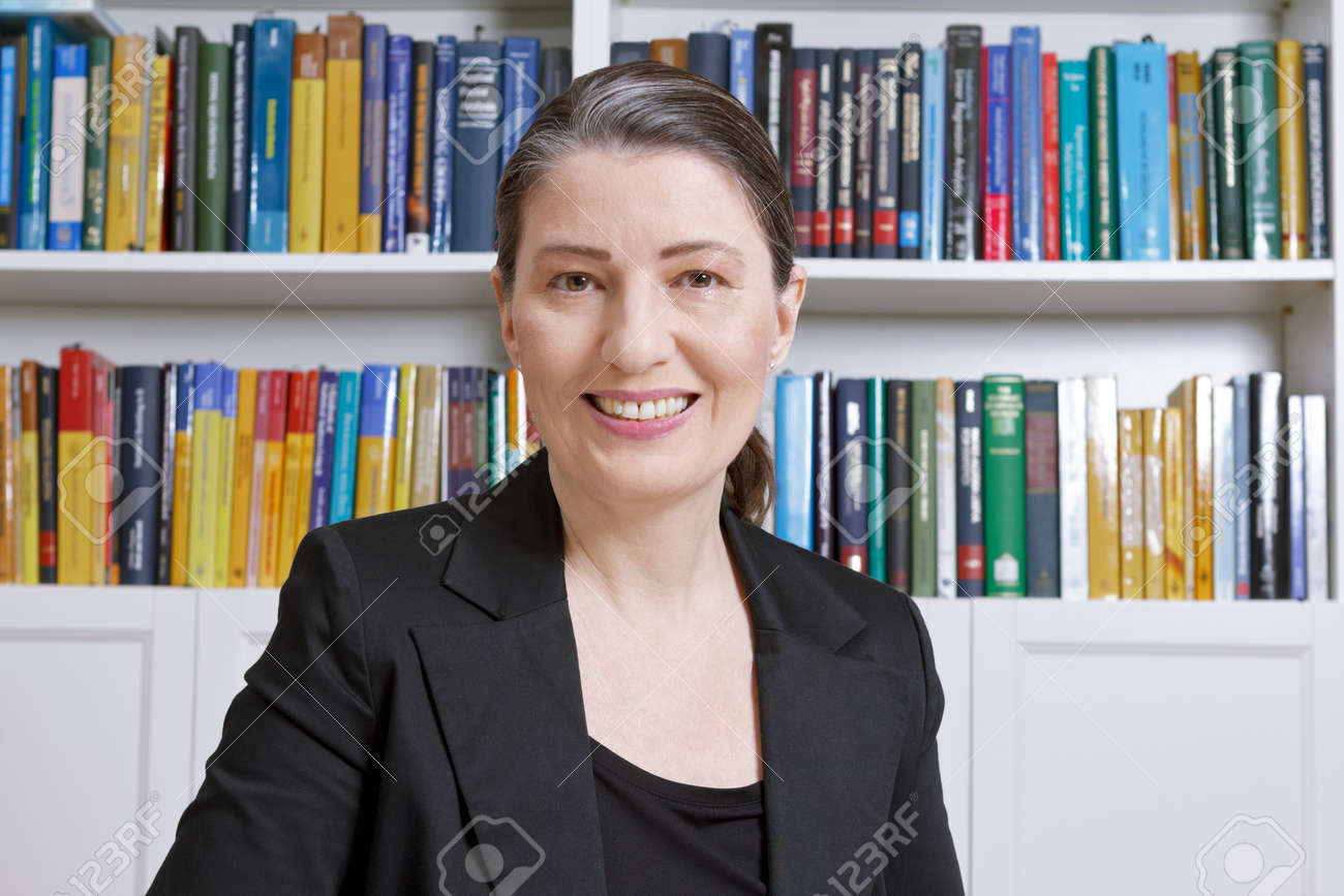 Friendly smiling mature woman with black blazer in an office with lots of books, professor, teacher, translator, lawyer, accountant or businesswoman - 73904550 Friendly smiling mature woman with black blazer in an office with lots of books, professor, teacher, translator, lawyer, accountant or businesswoman - 73904550