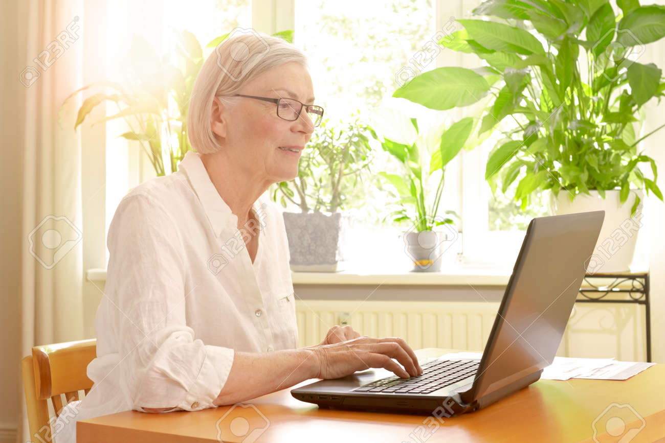 Happy senior woman in her sunny living room in front of her laptop enjoying the benefits of good financial planning for a carefree retirement - 81728554 Happy senior woman in her sunny living room in front of her laptop enjoying the benefits of good financial planning for a carefree retirement - 81728554