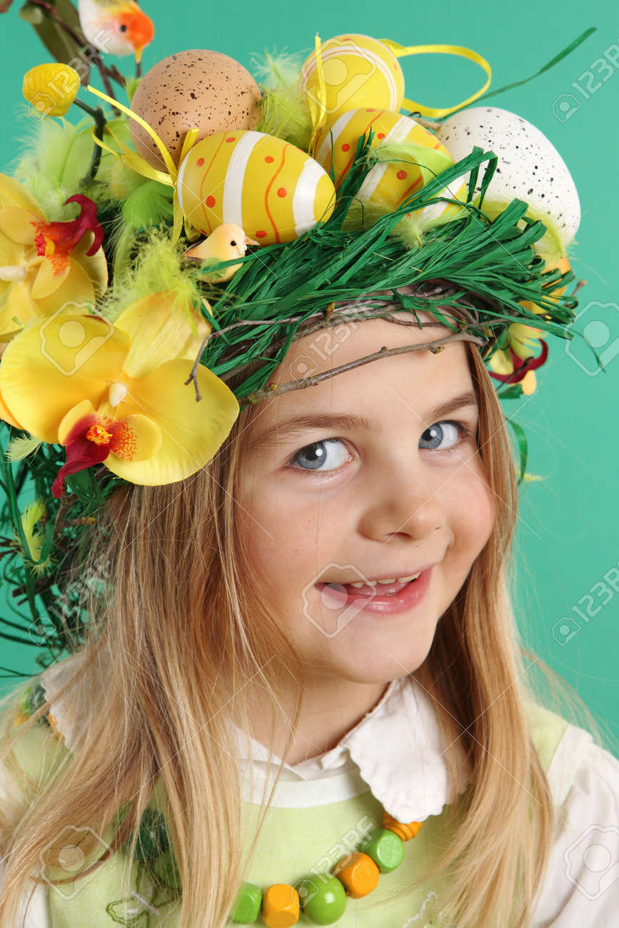 Portrait of a smiling blonde girl wearing hair dressing of yellow Easter eggs, spring flowers and bird feathers on a green background. The child looks at the camera - 166404000 Portrait of a smiling blonde girl wearing hair dressing of yellow Easter eggs, spring flowers and bird feathers on a green background. The child looks at the camera - 166404000