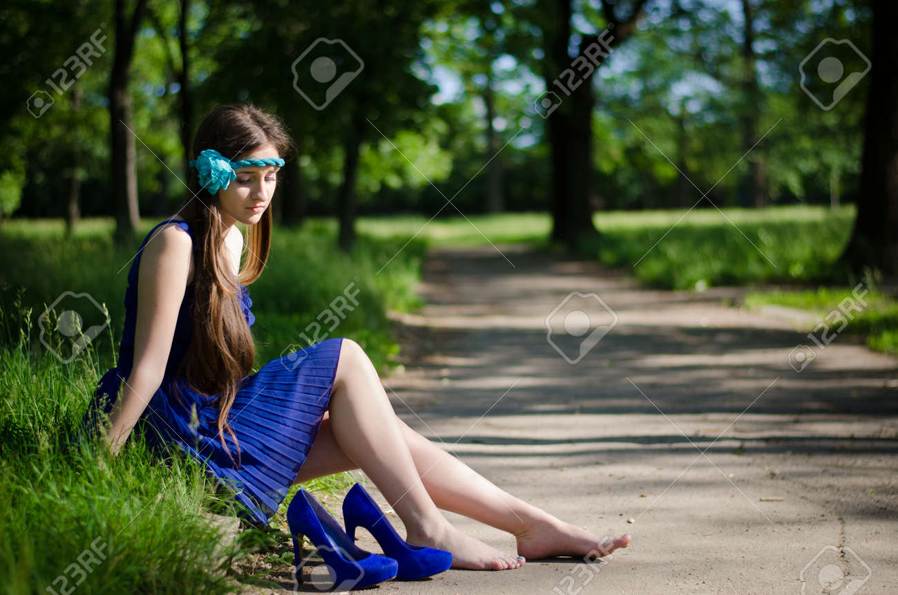 美しい少女の裸の足を彼女の靴を彼女の近くの道路の端に座っています の写真素材 画像素材 Image