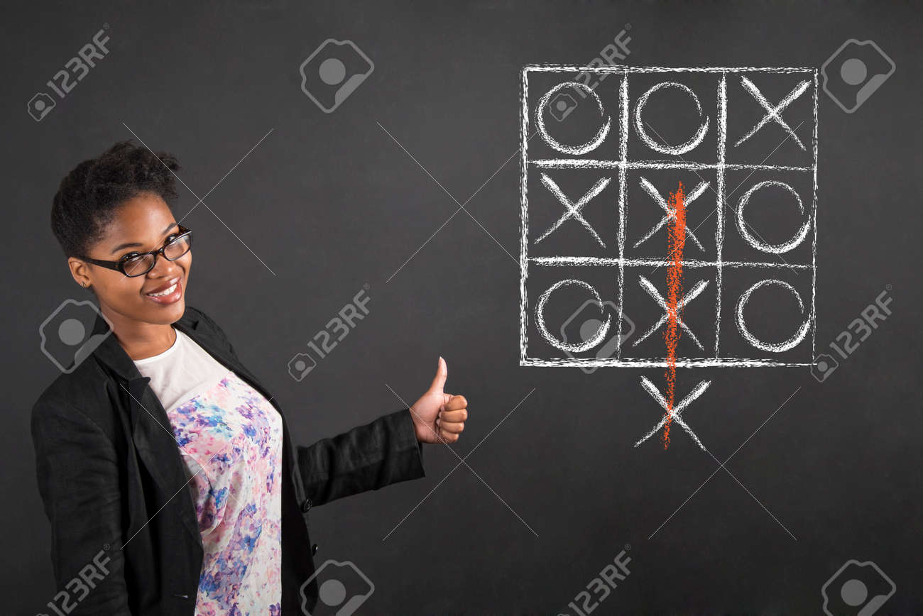 South African or African American black woman teacher or student with a thumbs up hand signal with tic tac toe standing against a chalk blackboard background inside - 45231853 South African or African American black woman teacher or student with a thumbs up hand signal with tic tac toe standing against a chalk blackboard background inside - 45231853