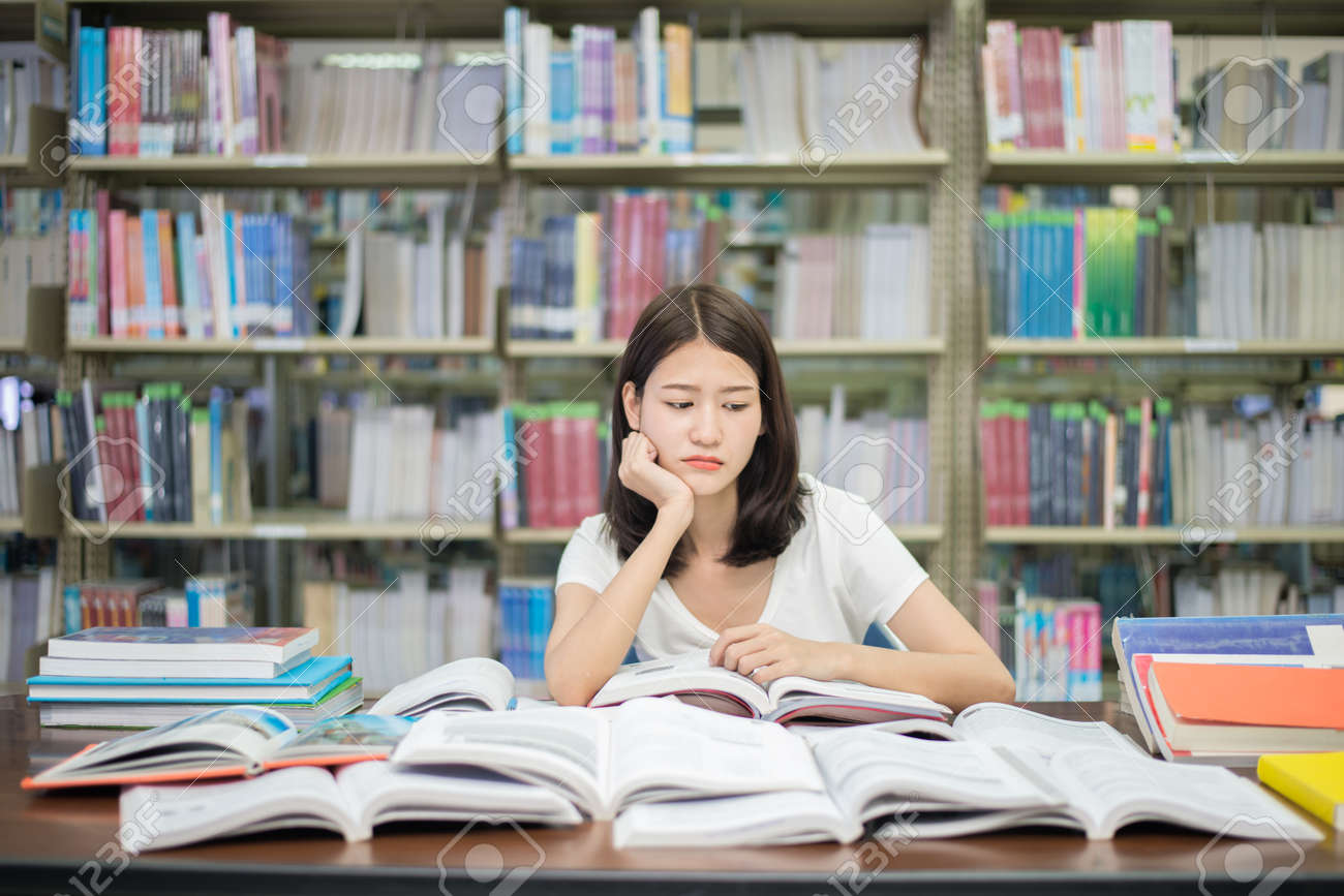Asian Woman Student Boring Reading Book At Library With A Lot Of Books In University. Asian Student Disheartened Reading Book For Examination. Stock Photo, Picture And Royalty Free Image. Image 81775975.