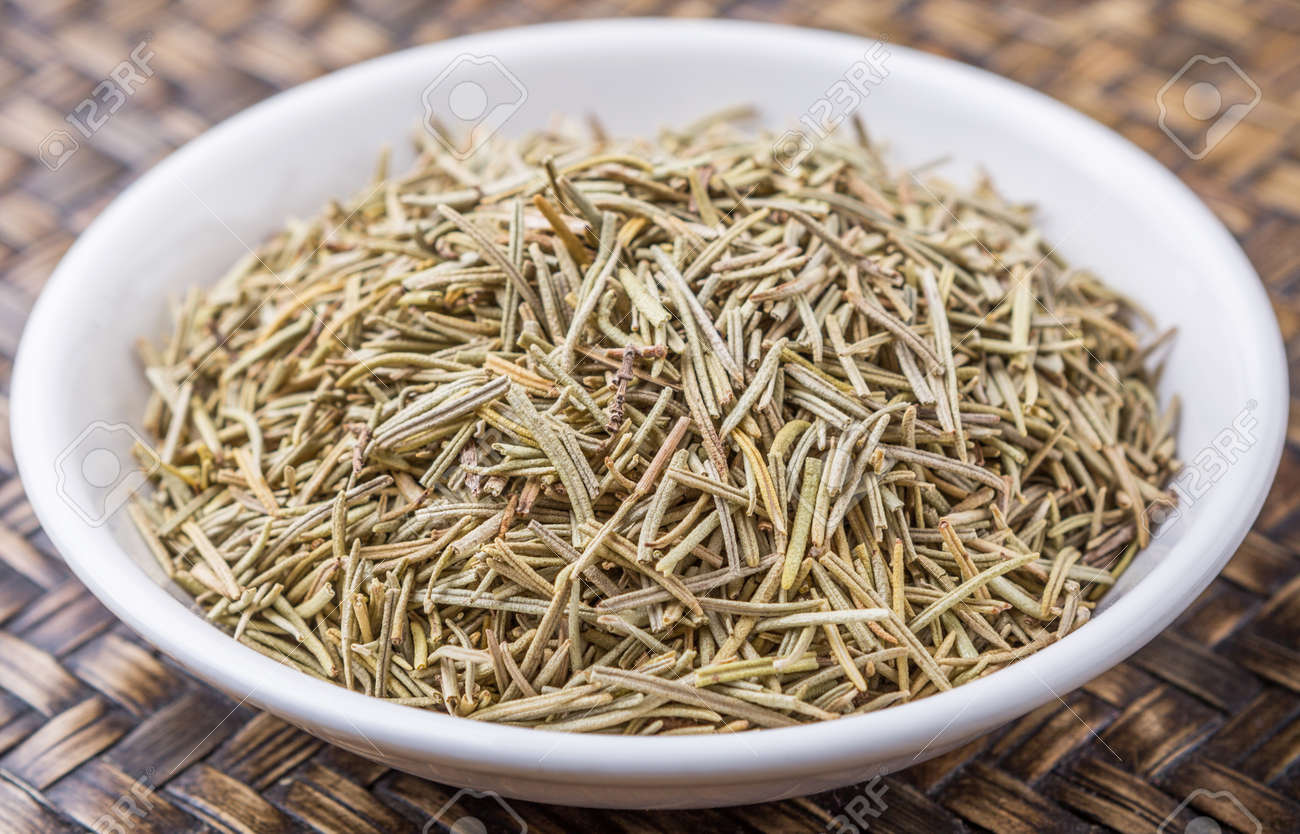 dried rosemary herb in white bowl on wicker background stock photo