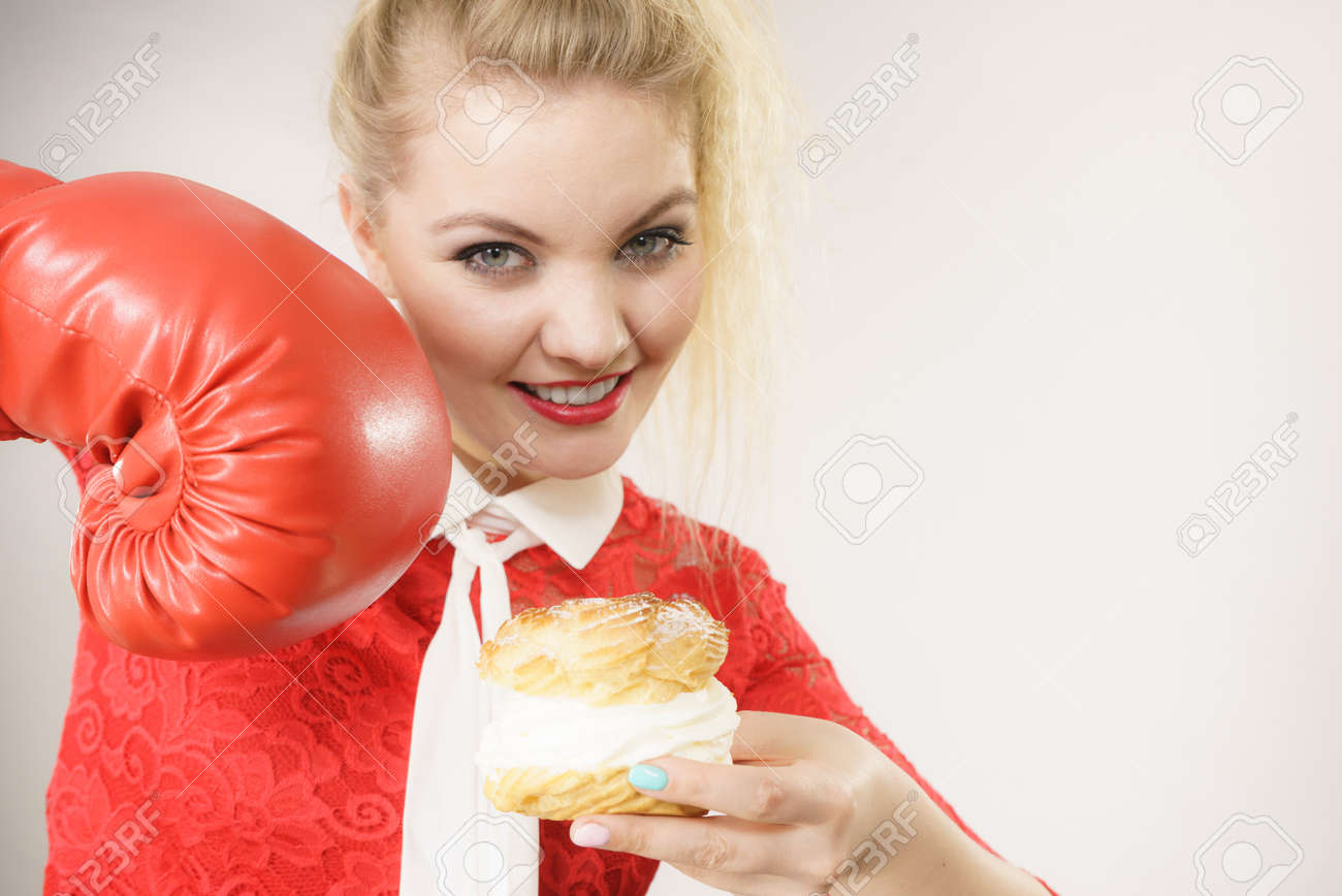 Regime Amaigrissant Concept De Perte De Poids Femme Blonde Drole Tenant Un Delicieux Gateau De Choux Avec Creme Fouettee Et Gant De Boxe Luttant Contre De Mauvaises Nourritures Sur Gris Banque D Images