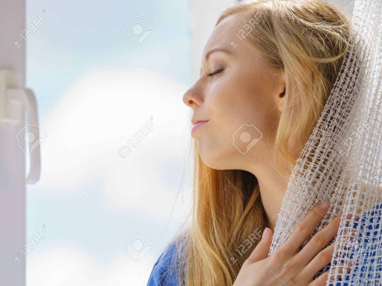 Happy woman with long blonde hair sitting on windowsill and relaxing, meditate or thinking holding white lace curtain. - 90618911 Happy woman with long blonde hair sitting on windowsill and relaxing, meditate or thinking holding white lace curtain. - 90618911